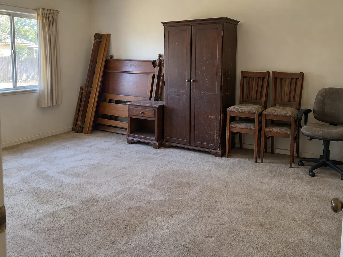 Spare bedroom with a wardrobe, bed frame, nightstand and chairs gathered for furniture removal
